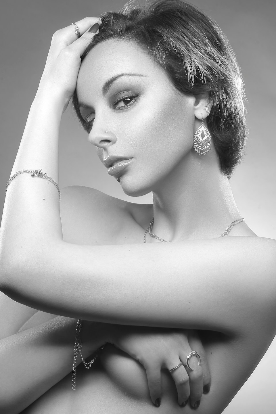 Woman with piercings and jewelry poses with hand on head.