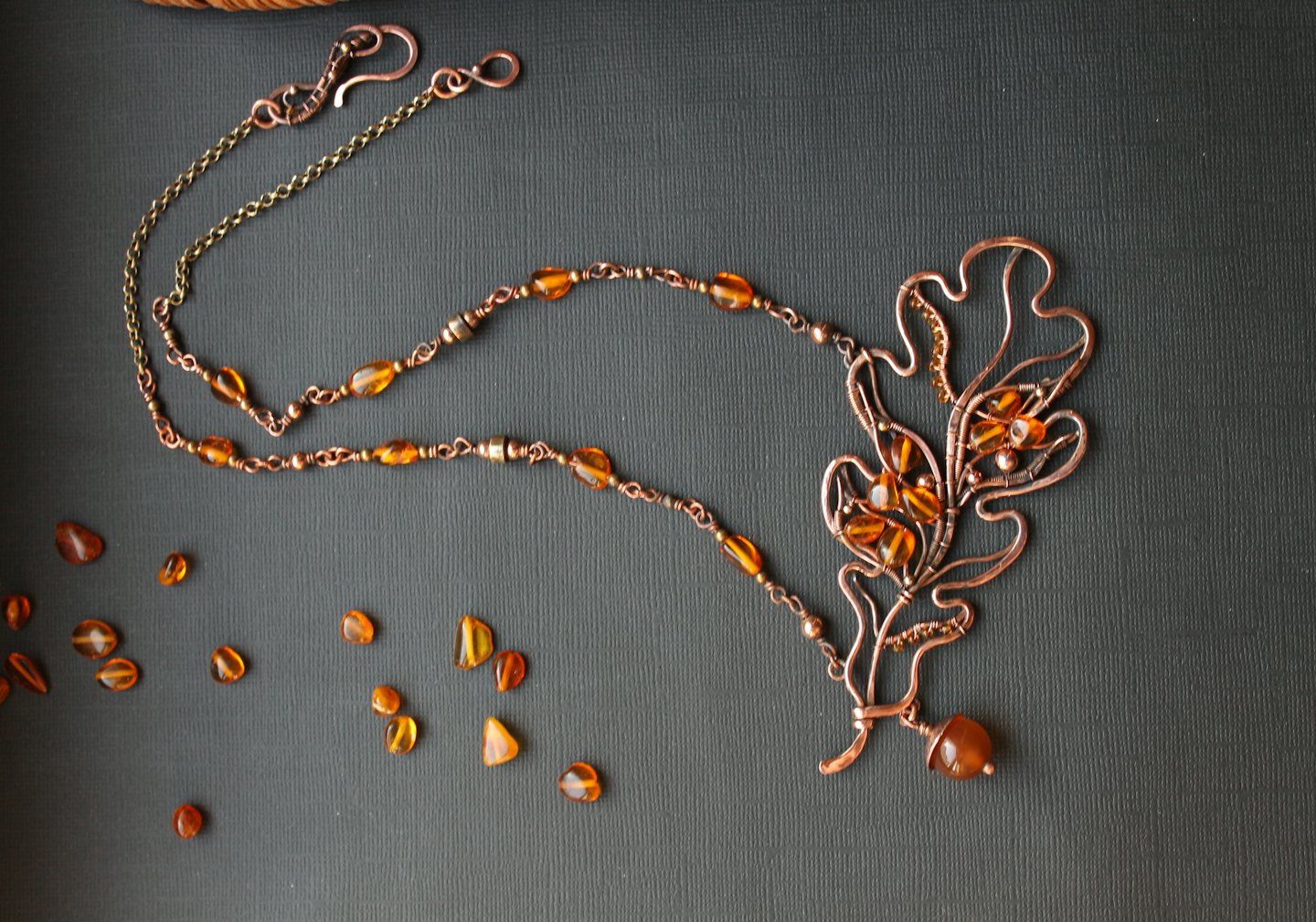 An oak leaf copper necklace with amber beads on textured grey.