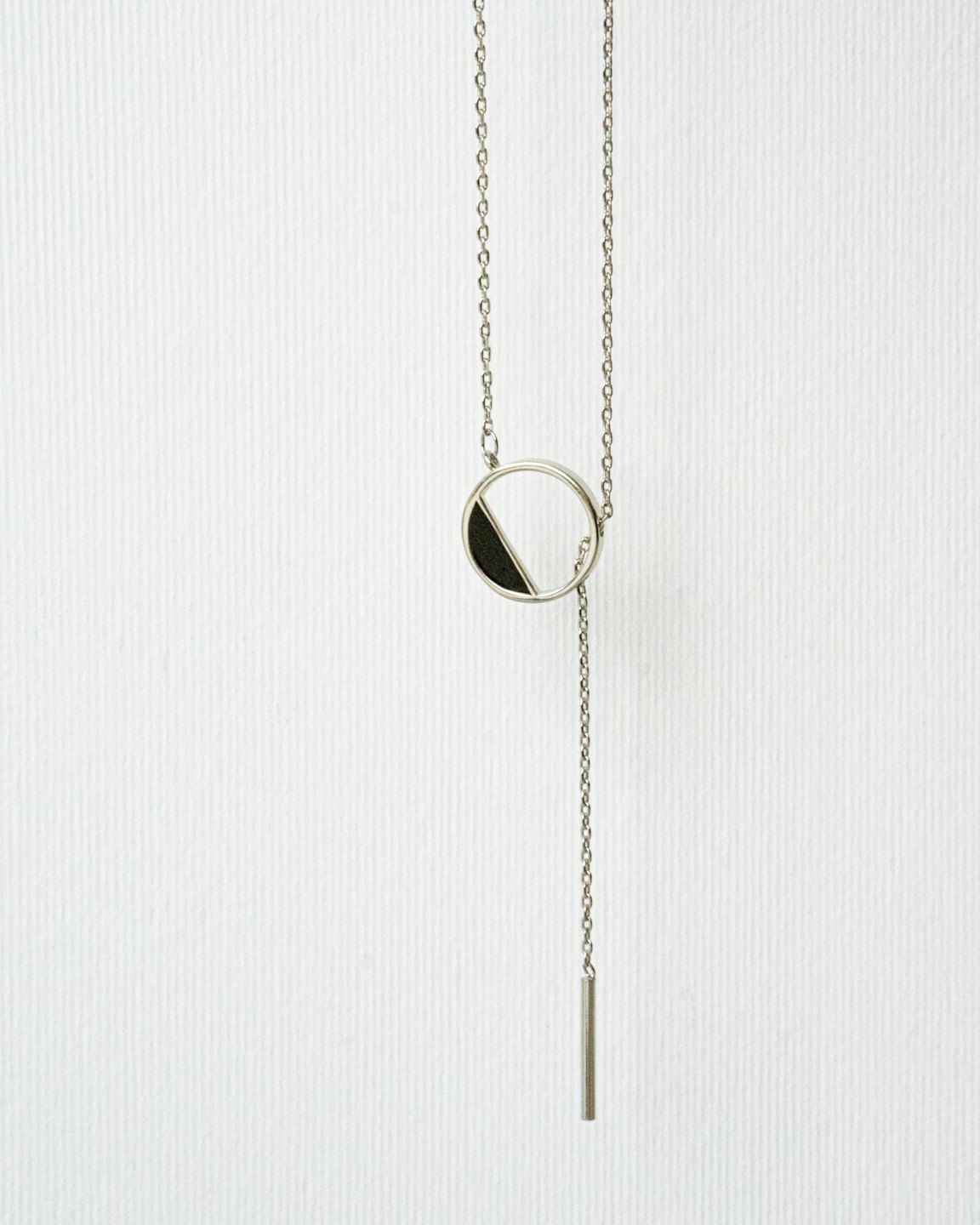 Silver necklace with a circular pendant and dangling bar.