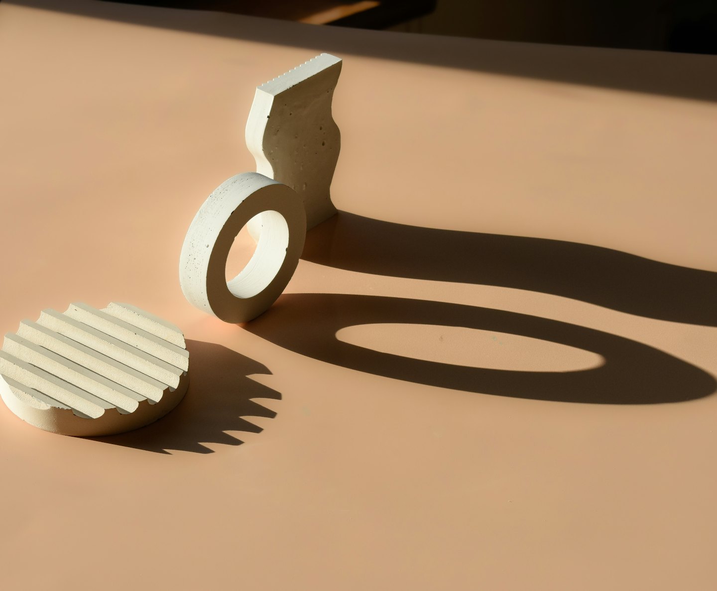 Abstract concrete shapes casting long shadows on a peach surface.