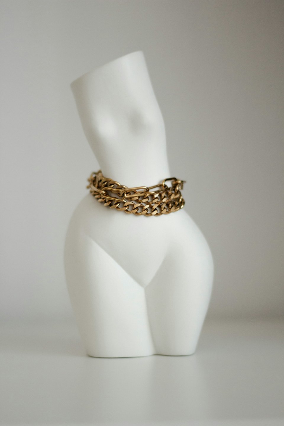 White abstract female torso bust wearing gold necklaces.