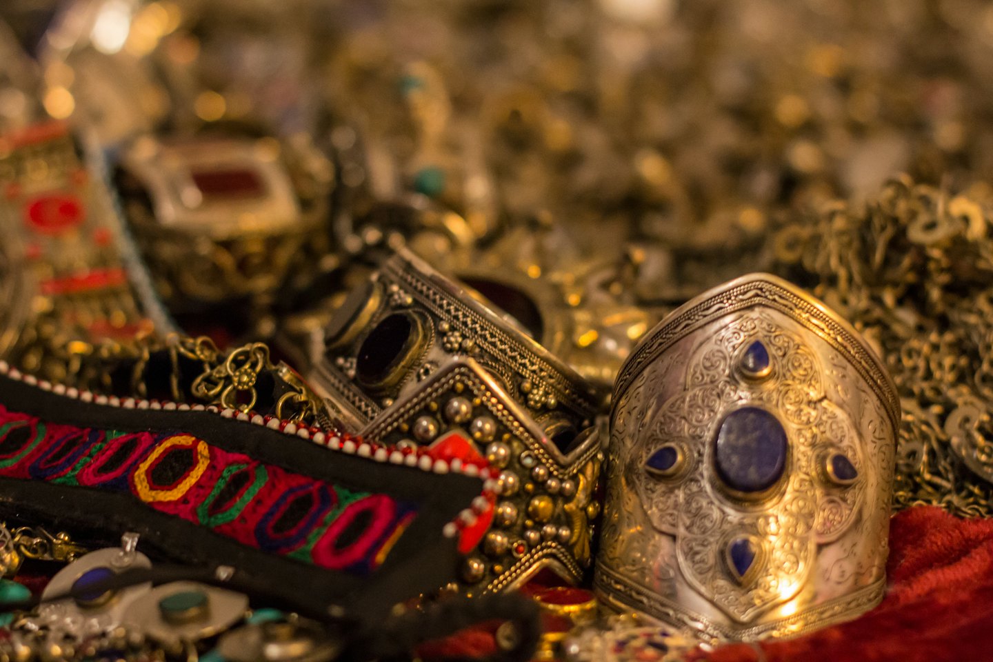 Ornate silver jewelry with gemstones on red fabric.