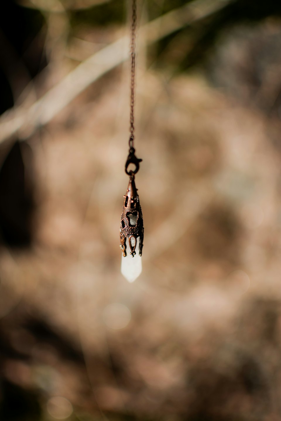 Bronze pendant with cutout details holding a crystal on a chain.