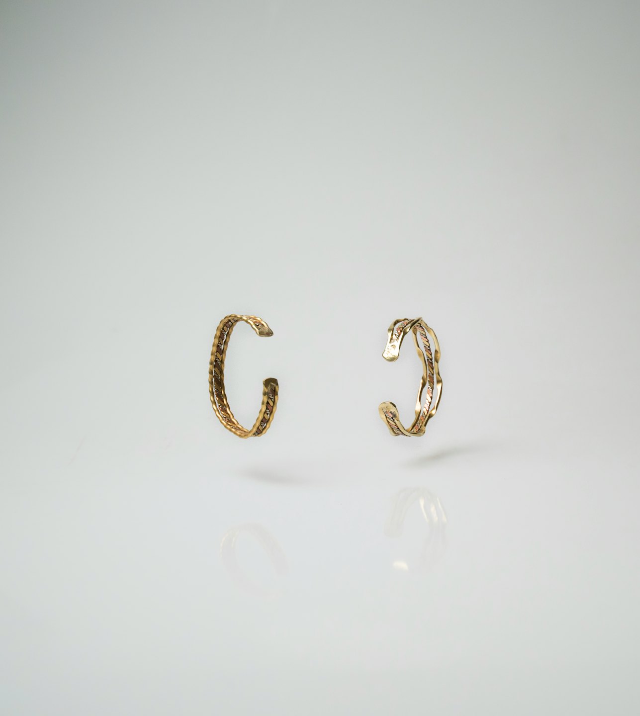 Two gold cuff bracelets on a white surface.