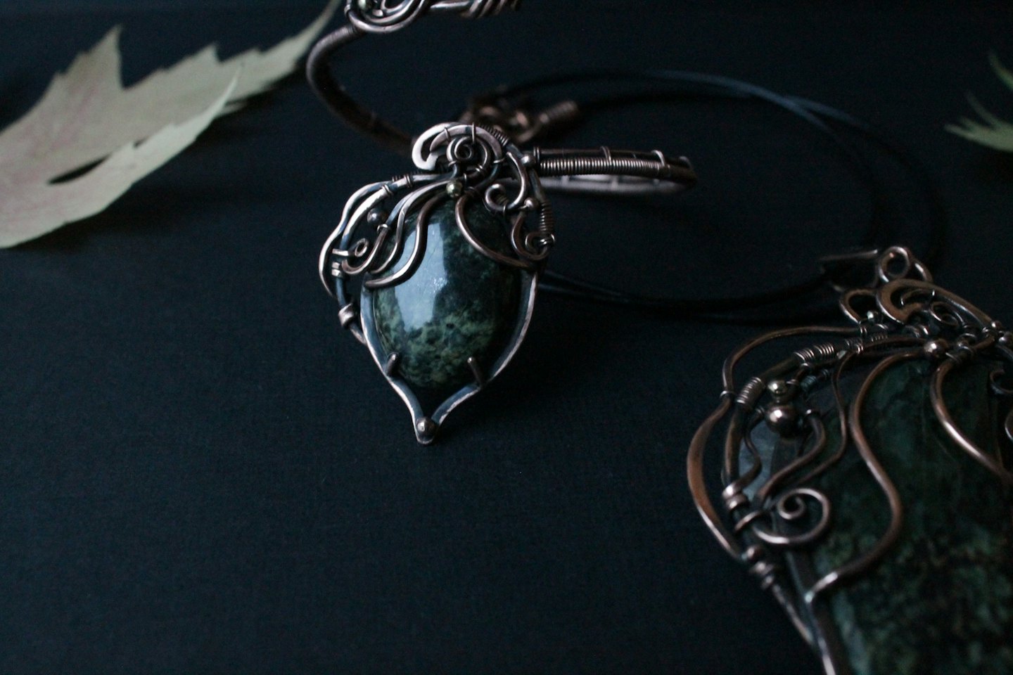 Two gemstone jewelry pieces wrapped in ornate copper wire.
