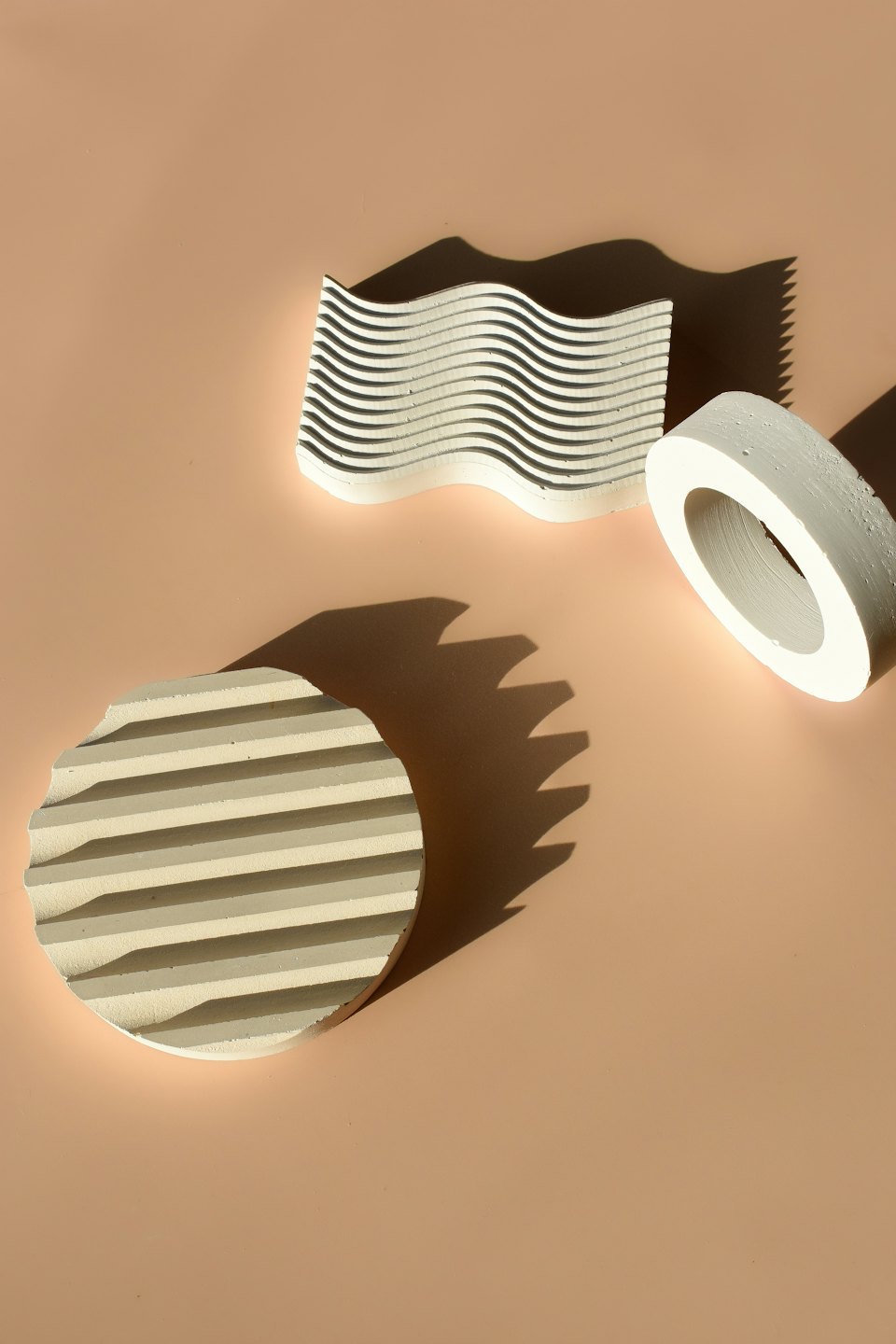 Three abstract concrete objects arranged on a peach surface.